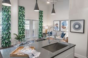 San Antonio apartment for rent - A modern kitchen with a sink, a window with curtains, and a dining table with glasses on it.