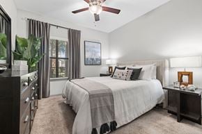 Katy apartment for rent - A bedroom with a large bed, a ceiling fan, and a window with curtains.