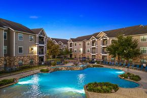 Katy apartment for rent - A swimming pool surrounded by a stone wall and chairs in front of apartment buildings.