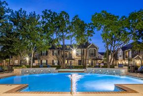 Houston apartment for rent - A swimming pool surrounded by trees and a building in the background.
