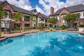 Houston apartment for rent - A large swimming pool in front of a brick building.