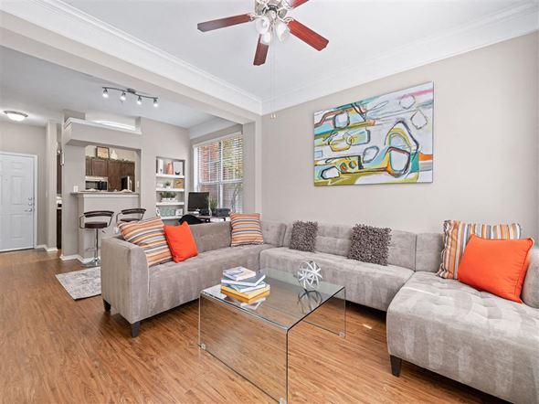 Dallas apartment for rent - A living room with a grey couch, a glass coffee table and a ceiling fan.