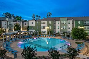 Huntsville apartment for rent - A swimming pool surrounded by lounge chairs and trees in front of apartment buildings.