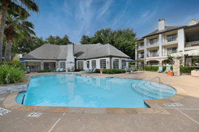Houston apartment for rent - A large swimming pool in front of a building with a patio and a tree.