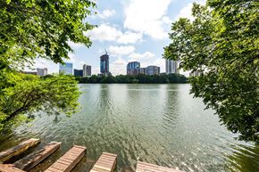 Austin apartment for rent - A serene lake with wooden docks and lush green trees in the foreground, with a city skyline in the background.