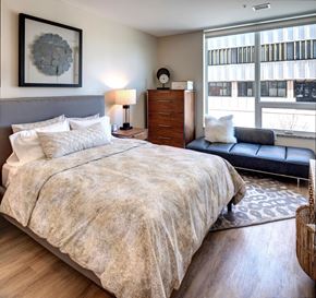 Kalamazoo apartment for rent - Downtown Kalamazoo Luxury Apartments - Spacious Bedroom With Wood-Inspired Plank Flooring, High Ceilings, And An Expansive Window With Views Of The Downtown Area