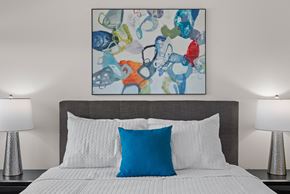 Mount Pleasant townhouse for rent - a bedroom with a bed with a blue pillow and a colorful painting above it at Tivoli Green Apartments & Townhomes, Mount Pleasant, WI