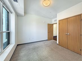 St. Paul apartment for rent - A room at The Lumin in the Highland Park neighborhood of St Paul with a carpeted floor, two wooden doors, and a window with a view of a building outside.