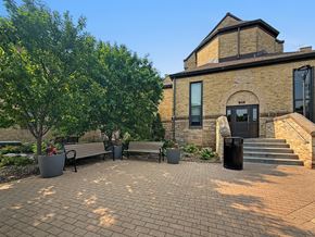Minneapolis apartment for rent - A brick building with a black door and windows is surrounded by trees and benches.