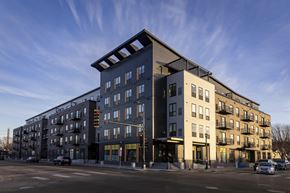 Minneapolis apartment for rent - A modern apartment building with a mix of dark and light facades is situated on a street corner with cars parked along the curb.