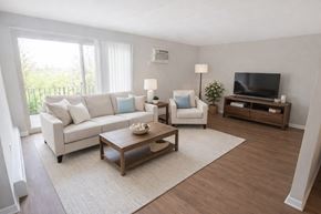 Cincinnati apartment for rent - A living room with a white couch, a white chair, a wooden coffee table, and a television.