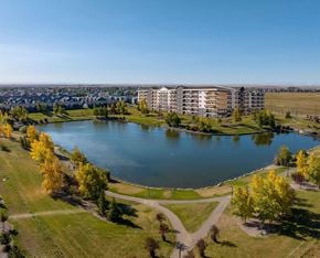 Lethbridge apartment for rent - A large building is situated next to a body of water with a grassy area in front of it.