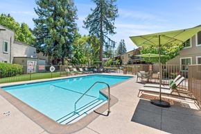 Walnut Creek apartment for rent - A swimming pool surrounded by trees and chairs under a yellow umbrella.