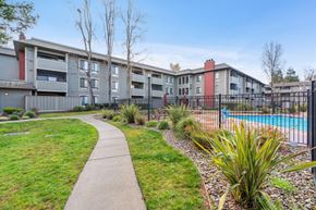 Martinez apartment for rent - A pool is surrounded by a fence and a grassy area with a walkway.