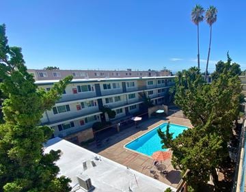 San Leandro apartment for rent - A pool surrounded by trees and a building in the background.
