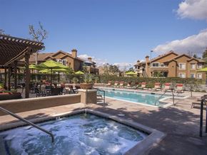 Foothill Ranch apartment for rent - A hot tub sits in the middle of a pool surrounded by chairs and umbrellas.