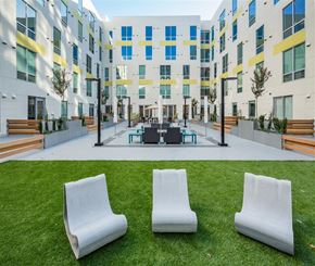 Sacramento apartment for rent - Three white chairs are placed on a green lawn in front of a building.