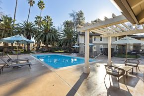 Livermore apartment for rent - A pool surrounded by palm trees and a patio area with chairs and a table.