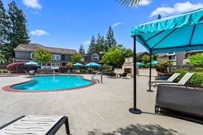 Rocklin apartment for rent - A pool area with a blue umbrella and a white bench.