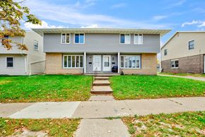 St Paul apartment for rent - A house with a grey facade and a white door is surrounded by a green lawn.