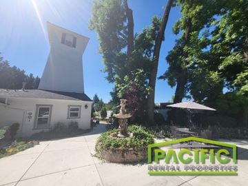 Medford apartment for rent - A white house with a tower-like structure on the roof is surrounded by greenery and has a sign that reads "PACIFIC RENTAL PROPERTIES".