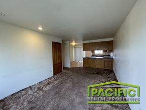 Medford apartment for rent - A spacious room with a carpeted floor and a wooden cabinet with a television on top.