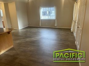 Grants Pass apartment for rent - A spacious room with wooden flooring and a window with white curtains.