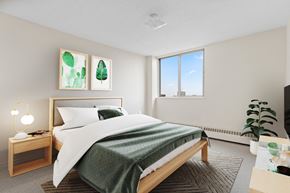 Regina apartment for rent - A bedroom with a large bed and a window overlooking a cityscape.