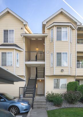 Spokane apartment for rent - a yellow apartment building with stairs and a blue car parked in front