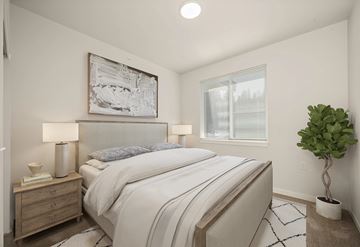 Spokane apartment for rent - A bedroom with a large bed, a nightstand with a lamp, a plant, and a framed artwork on the wall.