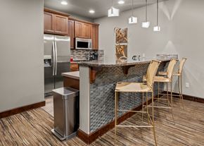 Spokane apartment for rent - A kitchen with a refrigerator, microwave, brown cabinets, and a bar with chairs.