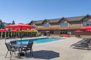 Spokane apartment for rent - A pool area with red umbrellas and chairs in front of a building.