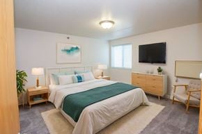 Fargo apartment for rent - A bedroom with a large bed, a chair, and a painting on the wall.
