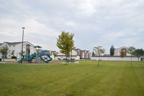 Fargo apartment for rent - A playground with a green slide and a tree in the middle of a grassy field.