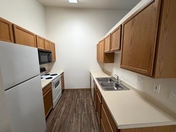 Fargo apartment for rent - A kitchen with a refrigerator, microwave, oven, sink and cabinets.