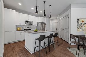 Colorado Springs apartment for rent - A kitchen with white cabinets and a white island with three black barstools.