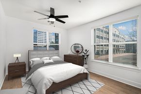 Centennial apartment for rent - A bedroom with a large bed, a ceiling fan, and a view of a cityscape through the window.