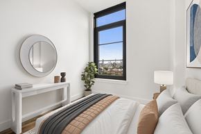 Queens apartment for rent - A bedroom with a large bed and a window overlooking a cityscape.