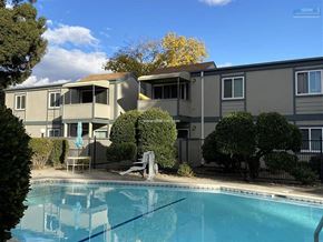 Chico apartment for rent - A swimming pool in front of a building with trees and bushes around it.
