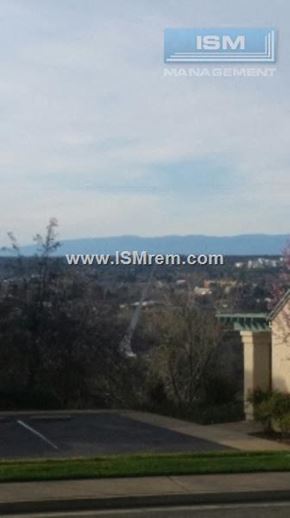 Redding apartment for rent - A view of a parking lot with a building and trees in the background.