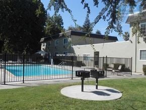 Turlock apartment for rent - A pool surrounded by a black fence with a bench in the middle of a grassy area.