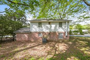 Forest Park house for rent - A white house with a brick foundation is surrounded by trees.