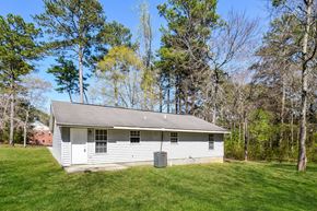 Conley house for rent - A small white house with a grey roof is surrounded by trees.