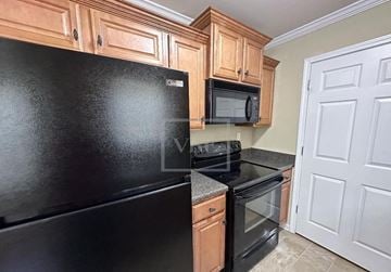 Adairsville house for rent - A black fridge and microwave in a kitchen with wooden cabinets.