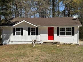 Jonesboro house for rent - A small white house with a red door stands alone in a grassy field.