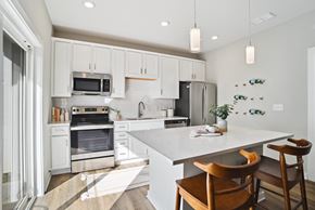 Charlotte triplex for rent - A kitchen with white cabinets and a white island with a wooden chair. at Zora University, Charlotte, NC, 28213