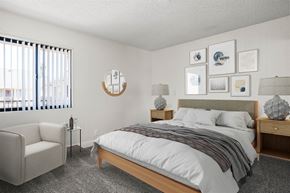 Anaheim apartment for rent - A bedroom with a bed, nightstand, chair, and pictures on the wall.
