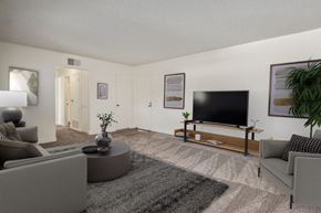 Anaheim apartment for rent - A living room with a grey sofa, a grey rug, a grey coffee table, a flat screen TV, and a potted plant.