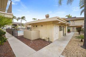 Anaheim apartment for rent - A house with a beige exterior and a brown roof is surrounded by a gravel area and a concrete walkway.