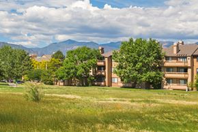 Colorado Springs apartment for rent - A grassy field in front of apartment buildings with trees and mountains in the background.